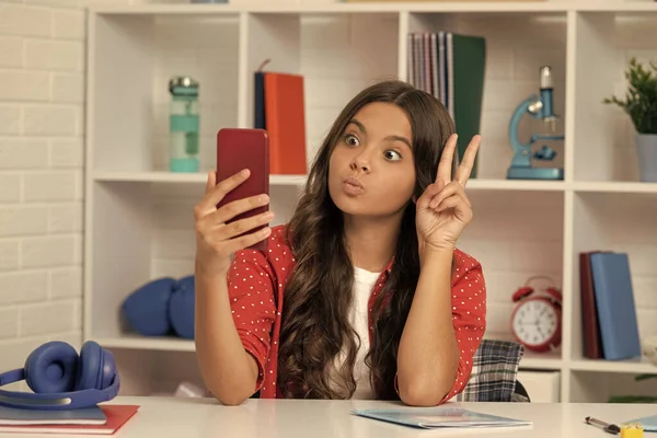 使用手机的Vlogger显示出和平姿态 快乐的少女博主使用智能手机 回学校去一个在教室里自作主张的孩子 9月1日儿童制作视频博客 手机博客 — 图库照片