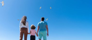 Deniz kıyısında kucaklaşan aile bayrağı. Yaz tatili, yatay afiş. Tatil gezisi geçmişi. Ebeveynler ve çocuk. Anne, baba ve oğul birlikte rahatlayın. Hayat sigortası