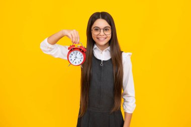 Mutlu kız yüzü, pozitif ve gülümseyen genç kız sarı arka planda saati tutuyor. Sabahın erken saatleri, günlük program. Çocuk kontrol zamanı. Geç kalmayın. Alarmı olan dakik bir çocuk. Son teslim tarihi