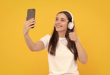 Kablosuz kulaklıkla giyin. Modern eğitim çevrimiçi. İletişim teknolojisi. Akıllı telefondan kadın sohbeti. Müzik dinliyordum. Başparmağını kaldır. Etkileyici bloglar. Kulaklıklı mutlu kız..