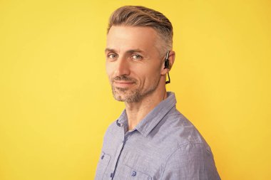 Sarı arka planda kablosuz kulaklık takan gülümseyen yetişkin adam, teknoloji.