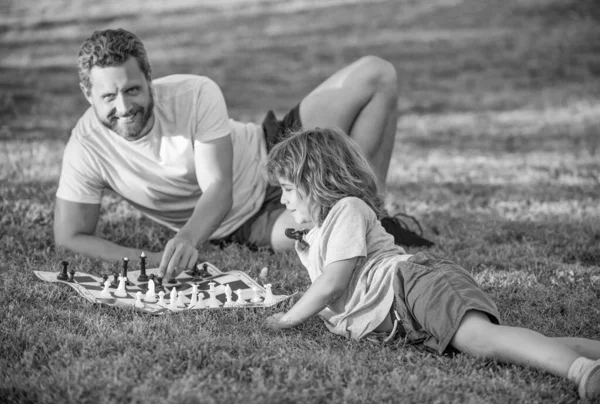 happy family of daddy and son child playing chess on green grass in park outdoor, checkmate.
