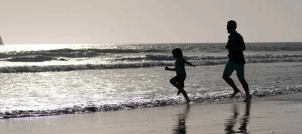 Silhouette of father and son run on summer beach outdoor, banner poster with copy space. Dad and child having fun outdoors. childhood and parenting. family holidays