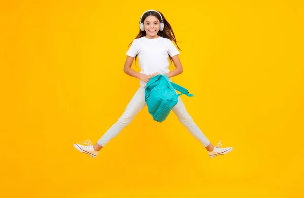 School teenager child girl in headphones with school backpack. Teenager student, isolated background. School leisure. Excited teenager, jump and run, jumping child