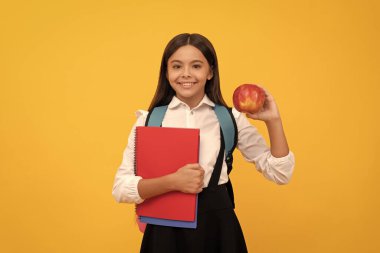 Happy kid go back to school holding apple and books yellow background, knowledge day.
