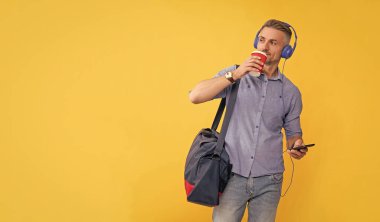 Adam kahve içerken kulaklıkla sohbet ediyor. kopyalama alanı. Kulaklıklı iş adamı seyahat çantalı akıllı telefon kullanır. Müziği dinle ve spor çantasını tut. modern hayat ve yaşam tarzı.
