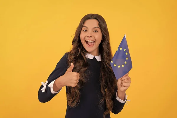 eurozone vacation. education in foreign school. thumb up. happy child holding european union flag on yellow background. touristic visa in schengen country. kid girl travel and studying abroad.