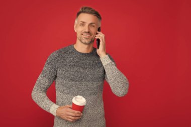 Mutlu adam fincandan kahve içiyor kırmızı arka planda telefonla konuşuyor, sohbet ediyor..