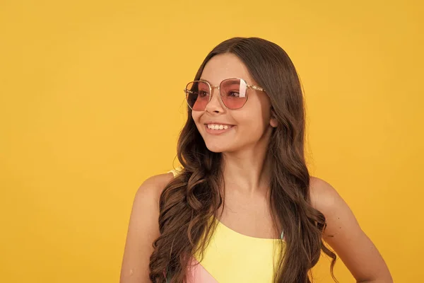 happy teen girl in summer glasses has curly hair on yellow background, summer portrait.