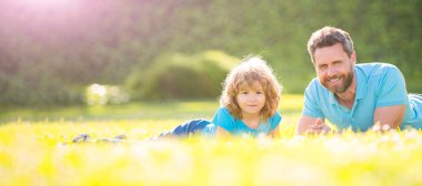 Açık yaz parkında baba ve oğulun bayrağı. Aile değeri. Çocukluk ve ebeveynlik. Ebeveyn rahat olsun. Küçük çocuk çimlerin üzerinde.