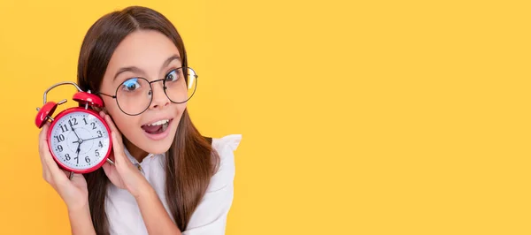 amazed child in school uniform and glasses listen alarm clock ringing showing time, amazement. Teenager child with clock alarm, horizontal poster. Banner header, copy space