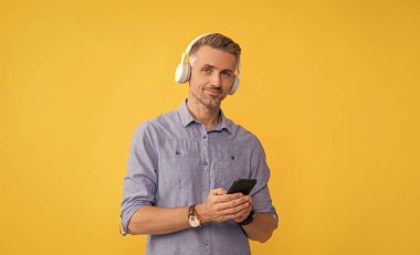 mobil müzik uygulaması. Yeni uygulama. Kulaklıklı adam akıllı telefondan konuşuyor. Müziği dinle ve telefonu tut. Modern hayat ve yaşam tarzı. Kulaklıkla konuşan bir adam. müzik çalma listesi.