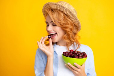 Kiraz meyvesi topluyorum. Sarıya izole edilmiş vişne tabağı olan hoş bir kadın.