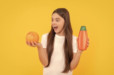 Şaşırmış çocuk duş jeli kullanıyor. Kuaförde uzun saç şampuanı. Saç kremi kullanan bir çocuk. Günlük alışkanlıklar ve kişisel bakım. Vücut bakımı kozmetik. Kız greyfurt şampuanı tutuyor. Gençler için kozmetik ürün sunumu