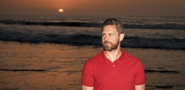 Gündoğumu plajındaki beyaz adam. Gömlekli sakallı adam. Yaz modası. Yaz tatili. pozitif duygular. Gün batımında deniz üzerinde sakallı yakışıklı bir adam. Sahildeki traşsız adam..