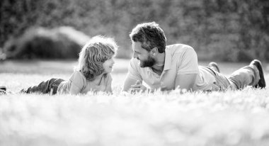 Mutlu baba ve oğul parkta eğleniyor. Aile değeri. Çocukluk ve ebeveynlik. Ebeveyn, küçük çocuk çimlerin üstündeyken rahatlar. Yazın çocuklu neşeli bir baba. Ebeveynlik ve babalık. Babalar Günü