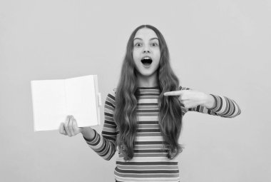 Bir göz at, bir kitap oku. Şaşırmış kız açık bir kitabı işaret ediyor. Edebiyat eğitimi. Edebiyat dersi. Okula dönelim. Başarılı olmak için oku, boşluğu kopyala.