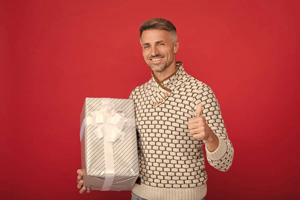 happy man in sweater hold present box on red background showing thumb up, birthday.