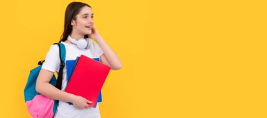 - Kız öğrenci. Sırt çantası ve kulaklıklı mutlu genç kız sarı arka plan ve bilgi kitapçığını tutuyor. İzole edilmiş yüz portresi, kopyalama alanı olan pankart