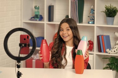 Şaşkın çocuk uzun kıvırcık saçlı bloglar için saç kremini gözden geçiriyor..