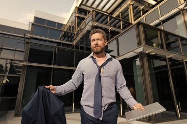 Dizüstü bilgisayarı olan dağınık bir iş adamı. Gömlekli ve kravatlı adam ceketini dışarıda tutuyor. İş gününden sonra girişimci. Erkek profesyonel traşsız CEO. Bilgisayarlı olgun patron. İş adamı ofis dışında..