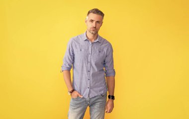 Sarı arka planda kol saati olan olgun bir adam, moda aksesuarı..