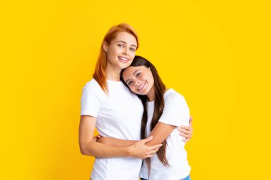 Güzel anne ve kız gülümsüyor mutlu bir şekilde sarılıyorlar izole edilmiş sarı arka planda.