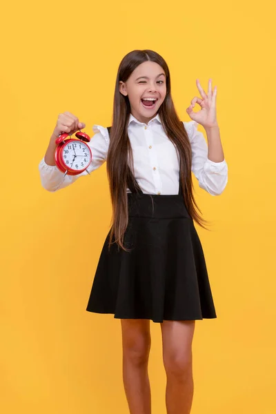 good morning. punctuality. last chance. ok gesture. punctual teen girl checking time. happy winking child with alarm clock. school kid in uniform showing time. you are late. deadline.