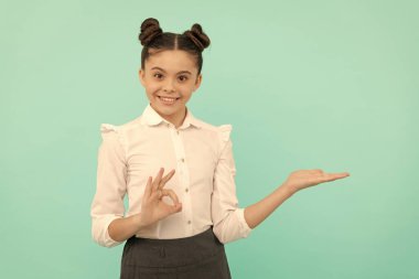 Mutlu liseli kız, tamam yüzük hareketi yapıyor. Ürünü tekrar okula tanıtmak için açık el hareketi yapıyor. Mavi arka plan fotokopi alanı, tatmin edici..