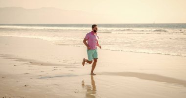 Yalınayak koşucu. Spor atleti deniz gündüz yarışını kazanmak için hızlı koşar. Sabah sporu aktivitesi. Güneşli sahilde koşan sağlıklı bir adam. Enerjik bir yaz. Koşucu özgürlüğü hisseder. Acele et. Dayanıklılık ve dayanıklılık.