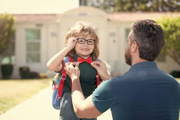 first day at school. father and son come back from school. happy family value. childhood and parenthood. parent gathering small child boy to first grade. nerd in eyewear with teacher. education.