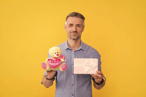 happy grizzled guy holding box and toy on yellow background, love.