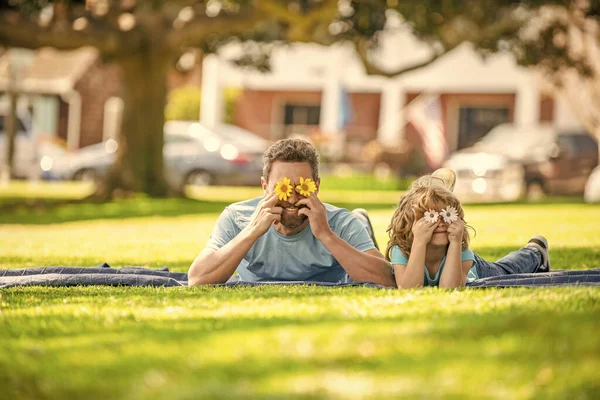 happy daddy with son play with flowers together on green park grass, family bonding.