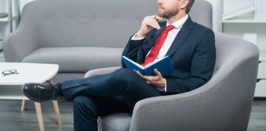 Takım elbiseli olgun bir işadamı okuma odasında oturup not defterine not alır..