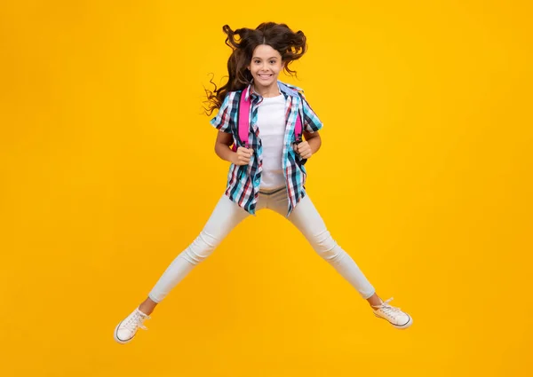Schoolgirl in school uniform with school bag. Crazy run and jump. Schoolchild, teen student hold backpack on yellow isolated background