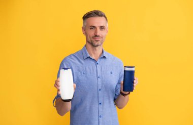 Sarı arka planda şampuan şişesi gösteren bir adam..