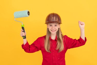 İnşaatçı şapkalı, sarı duvarında boya silindiri olan mutlu bir çocuk..