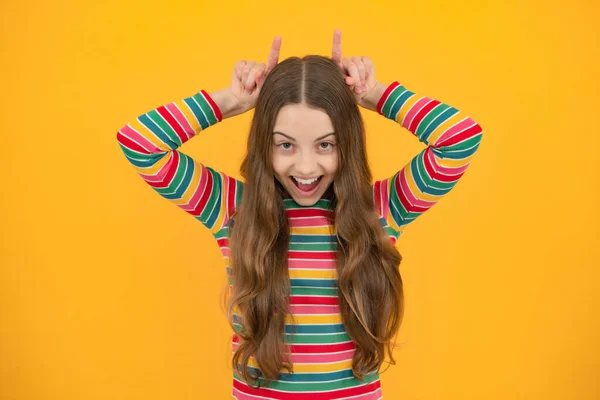 Excited face, cheerful emotions of teenager girl. Beautiful little girl doing funny gesture with finger over head as bull horns