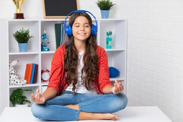 Mindfulness, meditation and relaxation concept. Teen girl with wireless headphones listening to relaxing music and meditating in lotus pose. Portrait of teen with headphone
