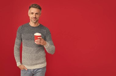 Güler yüzlü gri kazaklı adam kırmızı arka planda kahve içer, sabah.