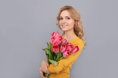 smiling woman with tulips. lady hold flowers for spring holiday. girl with bouquet on grey background. floral present for womens day. 8 march and mothers day.