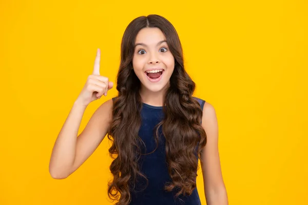 Excited face, cheerful emotions of teenager girl. Portrait of young teenager pointing up with finger, isolated on yellow background. Funny school girl, kid genius, nerd young student