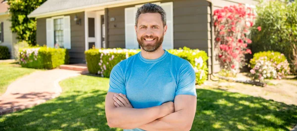 amazed unshaven guy crossed hands near house, realtor. Man face portrait, banner with copy space
