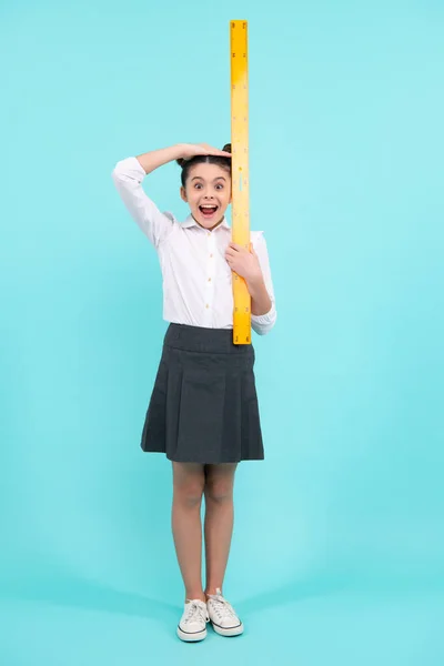Kid height measure, growth measurement. Schoolgirl in school uniform hold mathematics measure. Metric measurement. School equipment. Teenager student study stem disciplines. Excited teen girl
