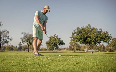 Yaz etkinliği. Profesyonel açık hava sporu. Profesyonel golf sahasında erkek golfçü. Golf sopasıyla şapkalı golfçünün portresi. İnsanların yaşam tarzı. Sportif adam yeşil çimlerde oyun oynuyor.