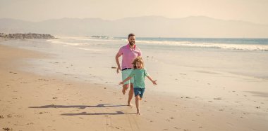 father and son running on summer beach. family travel weekend and vacation. childhood and parenting. daddy with kid boy in sea or ocean. weekend family day. healthy dad and child have fun outdoors.