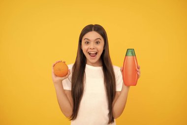 Sarı arka planda vücut losyonlu ve greyfurtlu uzun saçlı, şaşırtıcı genç kız, kozmetik.