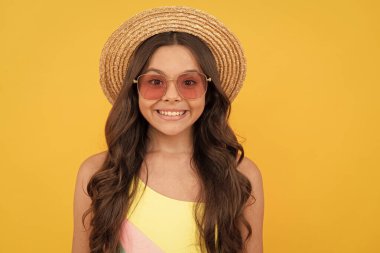 Yaz şapkalı ve gözlüklü mutlu çocuk sarı arka planda kıvırcık saçlı, yaz havasında..