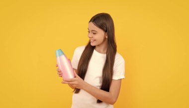 Mutlu çocuk sarı arka planda şampuan şişesi tut, güzellik..