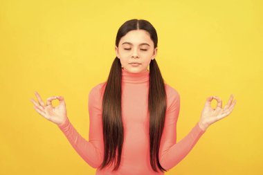 Uzun saçlı rahat çocuk sarı arka planda meditasyon yapıyor, yoga yapıyor..